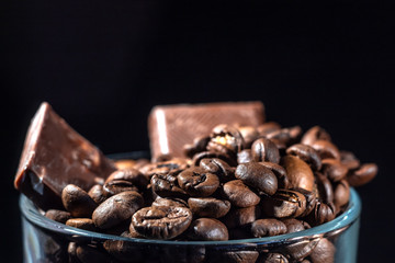 Glass cup of coffee with coffee beans and chocolate on a dark background, close-up in a low key