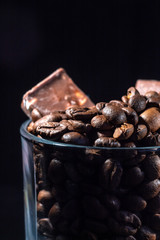Glass cup of coffee with coffee beans and chocolate on a dark background, close-up in a low key
