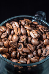 Glass cup of coffee beans on black background