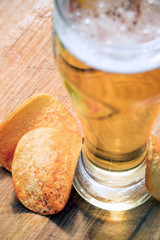 The beer style . glass of beer with potato chips on wooden background.