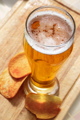The beer style . glass of beer with potato chips on wooden background.