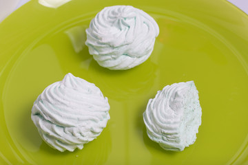 Homemade marshmallows laid on a plate. Marshmallow with mint, with a green tint. Nearby is a piece of marshmallow, its slice is visible. On the light green background.