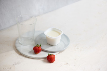 Fruit yogurt in plastic container with one strawberry on white background