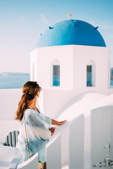 Fototapeta na wymiar Junge Frau schaut auf die weißen Häuser mit ihren blauen Kuppeln auf Santorini in Griechenland an 