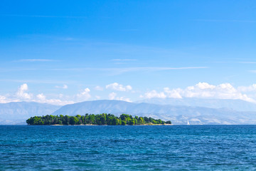Naklejka premium Wonderful romantic summertime panoramic seascape. Sailing yacht with white sails in to the crystal clear azure sea. Small green island against coastline slopes.