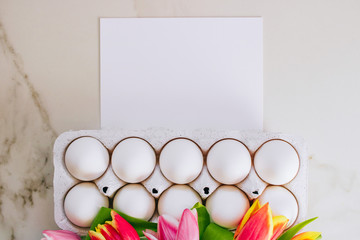 Easter concept, flat lay chicken eggs and white clean blank, colorful tulips on marble background. Top view.
