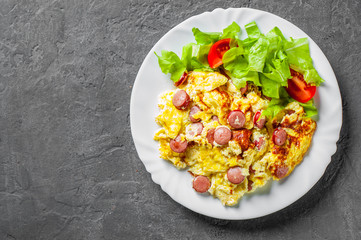 Omelet with sausage and vegetables in white plate on Dark grey black slate background