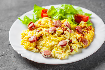 Omelet with sausage and vegetables in white plate on Dark grey black slate background