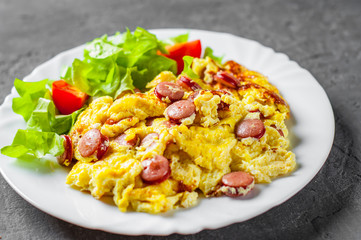 Omelet with sausage and vegetables in white plate on Dark grey black slate background