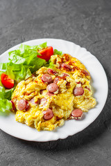 Omelet with sausage and vegetables in white plate on Dark grey black slate background