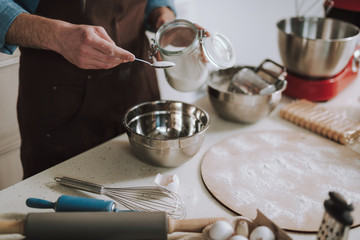 Hand holding jar of sugar and spoon above the bowl
