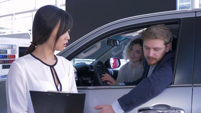 car seller Asian woman consult consumers young family sitting in auto salon while buying new car at showroom