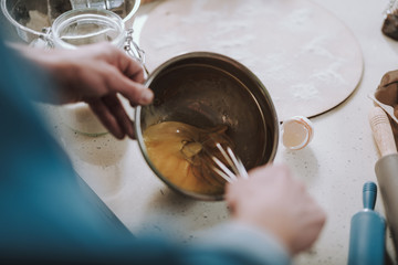 Top view of chicken eggs in the bowl and whisk in hand of person