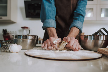 Strong hands of man kneading dough on the wooden cutting board