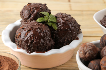 Chocolate ice cream with liquid chocolate and a mint leaf on a natural wooden background.