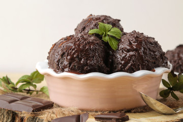 Chocolate ice cream with liquid chocolate and a mint leaf on a natural wooden background.