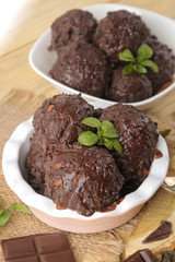 Chocolate ice cream with liquid chocolate and a mint leaf on a natural wooden background.