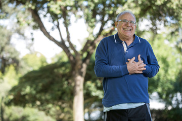 Uomo anziano con maglia blu sente un forte dolore al cuore mentre passeggia al parco