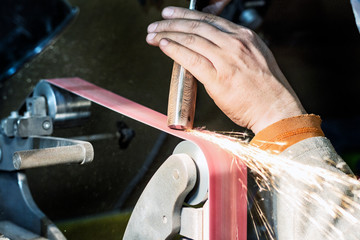 Obraz premium Making knife on the belt grinder with sparks, polishing, sanding handle 