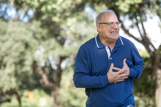 Uomo anziano con maglia blu sente un forte dolore al cuore mentre passeggia al parco
