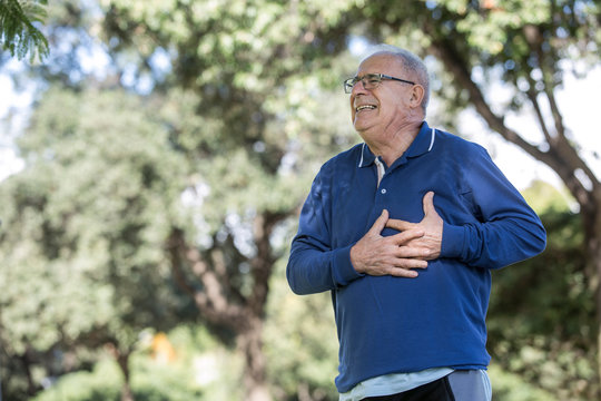 Uomo anziano con maglia blu sente un forte dolore al cuore mentre passeggia al parco