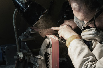 Obraz premium Making knife on the belt grinder with sparks, polishing, sanding handle 