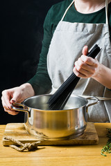 Fototapeta na wymiar The chef puts black spaghetti in boiling water. Black background, side view, kitchen