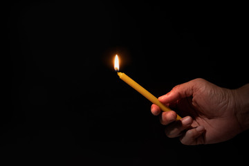 Hand holding yellow burning candle on black background