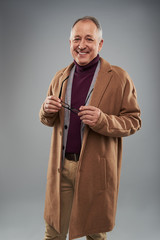 Cheerful man in long coat standing alone and holding glasses