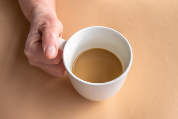 Elderly woman holds morning coffee with milk in hand.