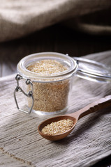 Raw organic superfood gluten free quinoa seeds in wooden spoon and glass airtight jar on kitchen table closeup