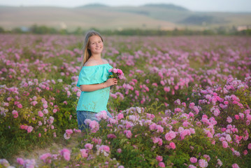 Young beautiful blonde girl on a rose plantation . She is holding a bouquet of pink roses