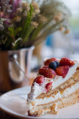 A Piece of Pavlova Cake decorated by some chop of strawberries on a white plate.