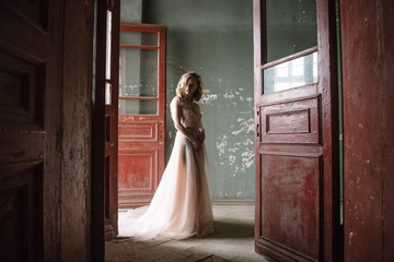 Young woman posing in a pink tender light long dress indoors