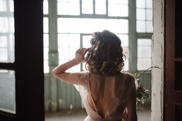 Young woman posing in a pink long dress backs indoors