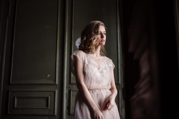Obraz na płótnie Canvas Young woman posing in a pink tender light long dress indoors