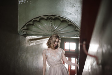 Young woman posing in a pink tender light long dress indoors