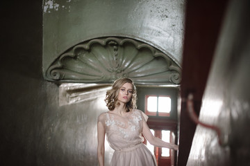 Young woman posing in a pink tender light long dress indoors