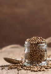 Coriander seeds in jar, dry oriental spice, rustic style, old kitchen table, selective focus