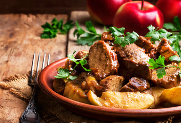 Hot pork stew with apple slice on the plate, vintage wooden kitchen table background, selective...