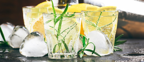Refreshing cool summer lemon drink with rosemary, ice and gin tonic, black stone bar counter...