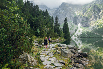 Back view of young women in sportswear hiking on the stony pathway, and cliffs in mountains. Morskie Oko lake, High Tatras, Zakopane, Poland.
