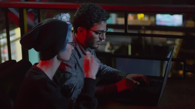 Medium shot of male hacker coding on laptop and young woman sitting nearby telling him what to do