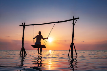 Happy girl relaxing at the beach on rope swing above sea water at sunset, summer vacation holidays...
