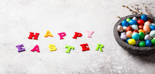 Easter holiday concept.Painted eggs in a plate on a gray background. Holiday decorative willow branches. Inscription in colored letters.