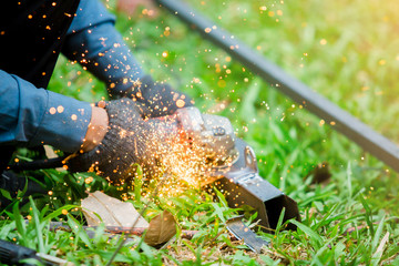 hands of worker grinding or cutting metal with grinder at outdoor lawn or construction site