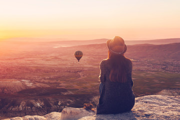 A woman on top of a hill alone admires the tranquil natural landscape and balloon and enjoys...
