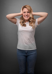 Attractive woman covers her ears with her hands on a gray background.