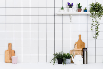 Various kinds of kitchen tools arranged on the white table. And tidy flower pots are placed neatly on the shelf.