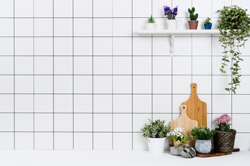 Various kinds of kitchen tools arranged on the white table. And tidy flower pots are placed neatly on the shelf.